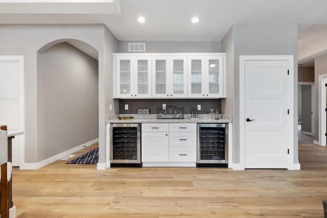 bar with light stone counters, beverage cooler, light hardwood / wood-style flooring, and white cabinets