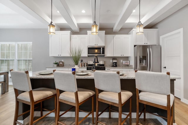 kitchen featuring stainless steel appliances, an island with sink, white cabinetry, and beam ceiling