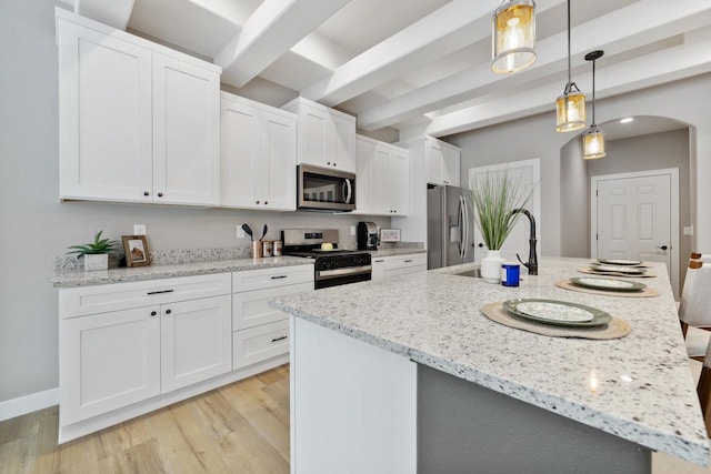 kitchen with decorative light fixtures, stainless steel appliances, an island with sink, and white cabinets