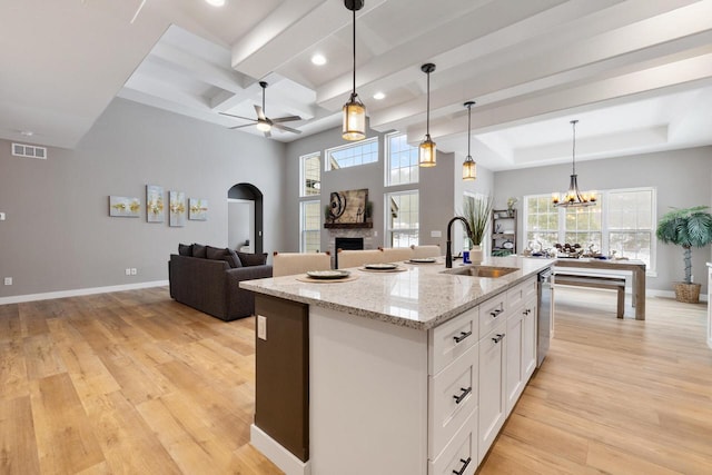 kitchen featuring sink, hanging light fixtures, light stone counters, an island with sink, and white cabinets