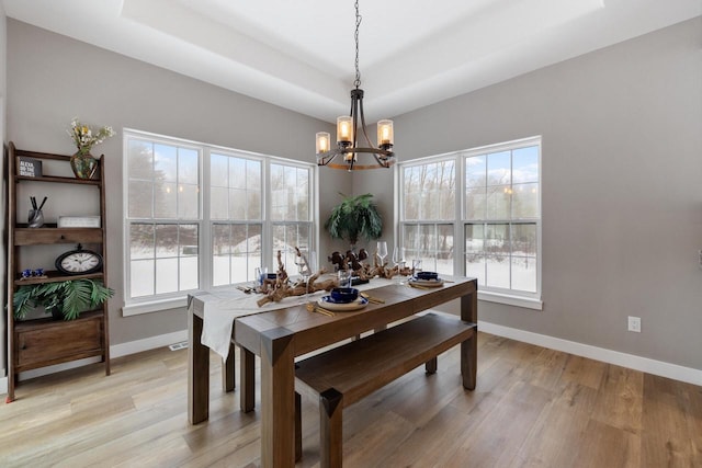 dining room with a notable chandelier, light hardwood / wood-style flooring, and a raised ceiling