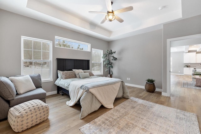 bedroom featuring ceiling fan, a raised ceiling, and light wood-type flooring