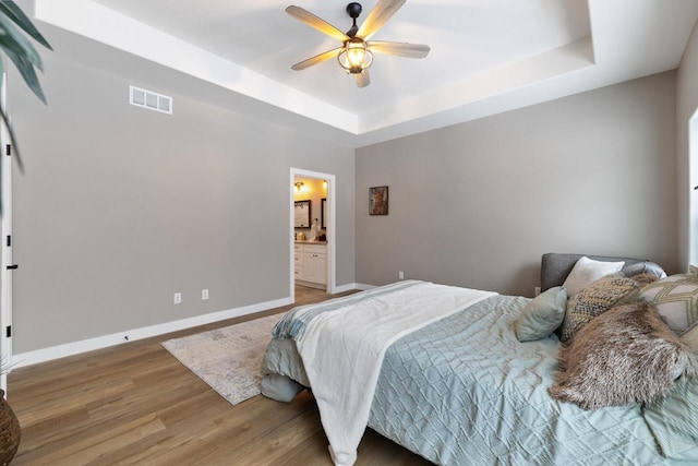 bedroom with hardwood / wood-style floors, a tray ceiling, ceiling fan, and ensuite bathroom