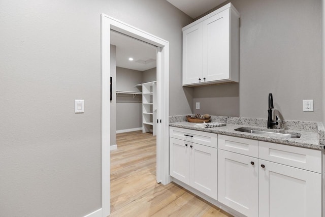 interior space featuring sink, light stone countertops, light hardwood / wood-style floors, and white cabinets