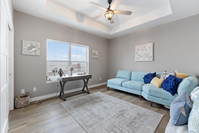 living room featuring a tray ceiling, light hardwood / wood-style flooring, and ceiling fan