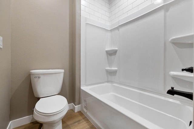 bathroom featuring hardwood / wood-style flooring, washtub / shower combination, and toilet