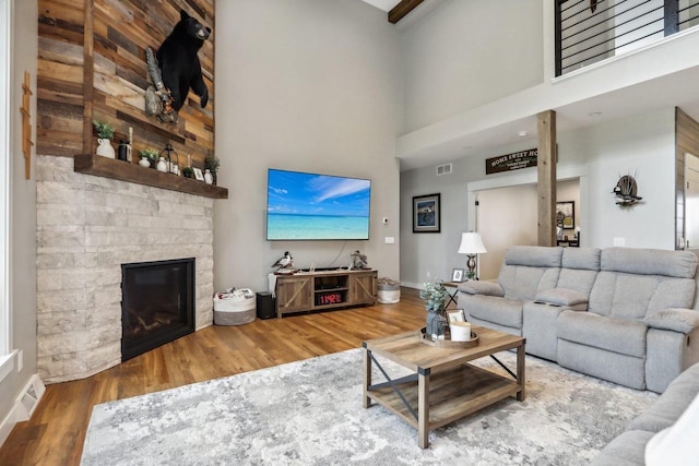 living room with a towering ceiling, a stone fireplace, and hardwood / wood-style flooring