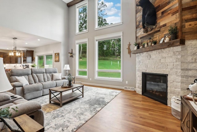 living room with a high ceiling, plenty of natural light, a stone fireplace, and light hardwood / wood-style flooring