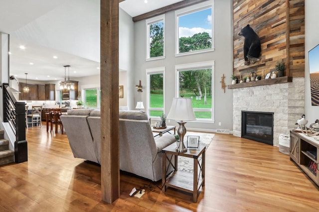 living room with an inviting chandelier, a towering ceiling, a fireplace, and light wood-type flooring