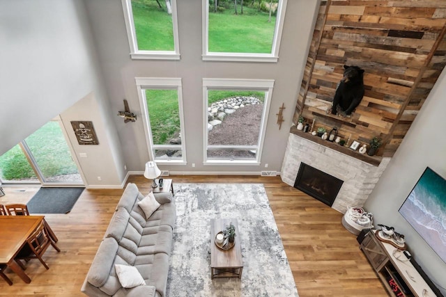 living room featuring a towering ceiling, a stone fireplace, and light hardwood / wood-style floors