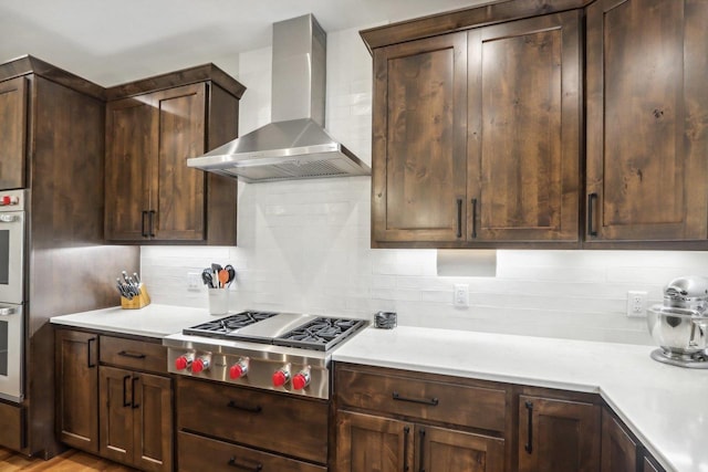 kitchen with backsplash, stainless steel gas cooktop, dark brown cabinets, and wall chimney range hood