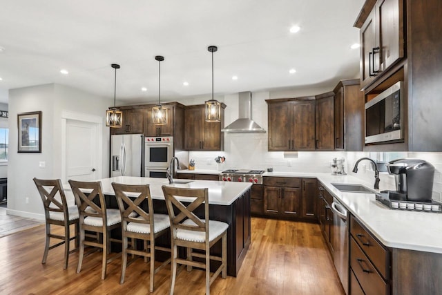 kitchen with sink, appliances with stainless steel finishes, a kitchen island, pendant lighting, and wall chimney range hood