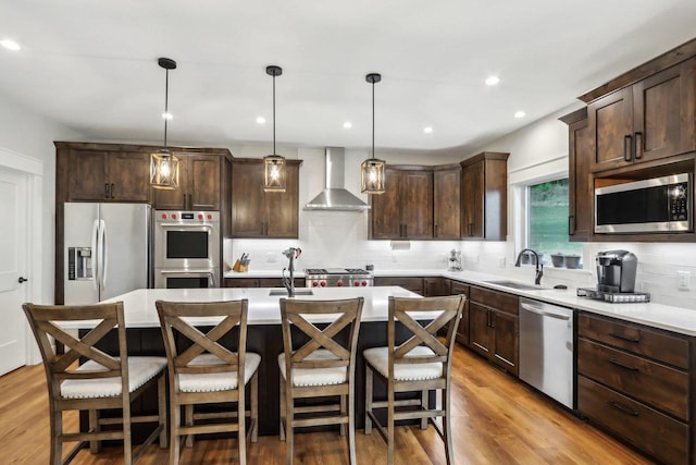 kitchen featuring wall chimney range hood, stainless steel appliances, hanging light fixtures, and a center island