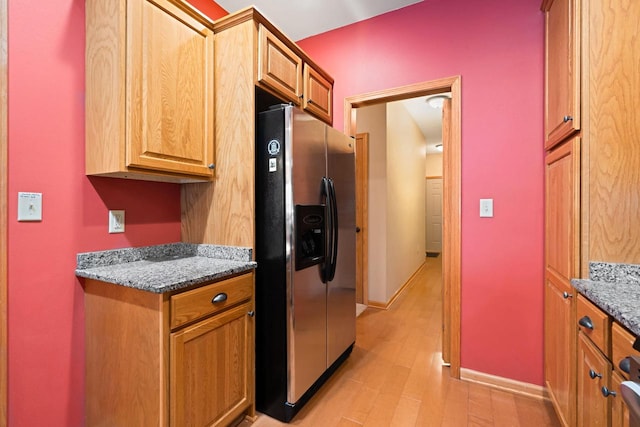 kitchen with dark stone counters, stainless steel fridge with ice dispenser, and light wood-type flooring