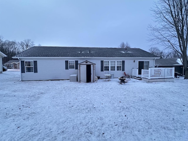 snow covered property with a wooden deck, a storage shed, and an outdoor fire pit