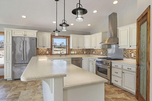 kitchen with a kitchen island, pendant lighting, sink, premium appliances, and wall chimney range hood