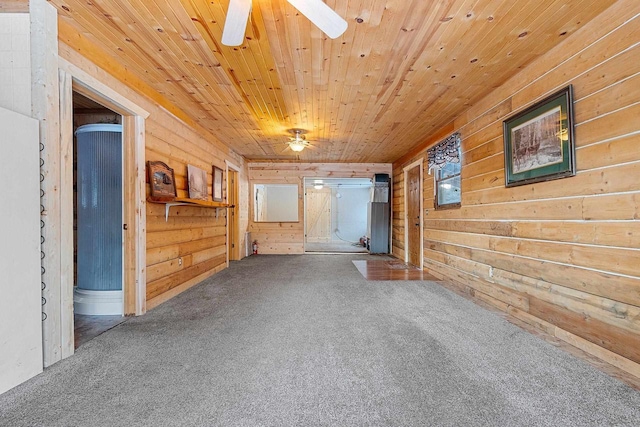 carpeted empty room featuring wood ceiling, ceiling fan, and wooden walls