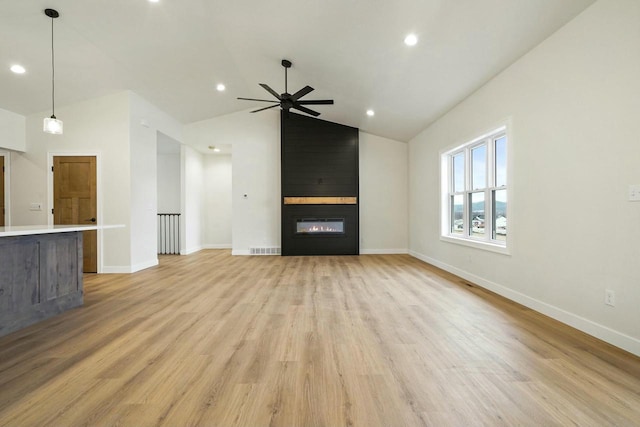 unfurnished living room with ceiling fan, lofted ceiling, a large fireplace, and light wood-type flooring