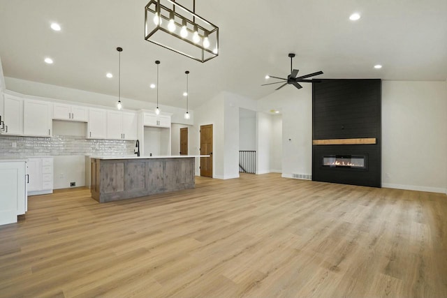 kitchen with white cabinetry, tasteful backsplash, a fireplace, decorative light fixtures, and a large island with sink