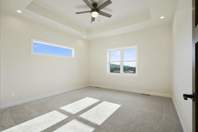 unfurnished room with a raised ceiling, light colored carpet, and ceiling fan