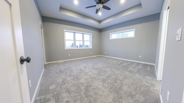 spare room featuring a raised ceiling, light carpet, and ceiling fan