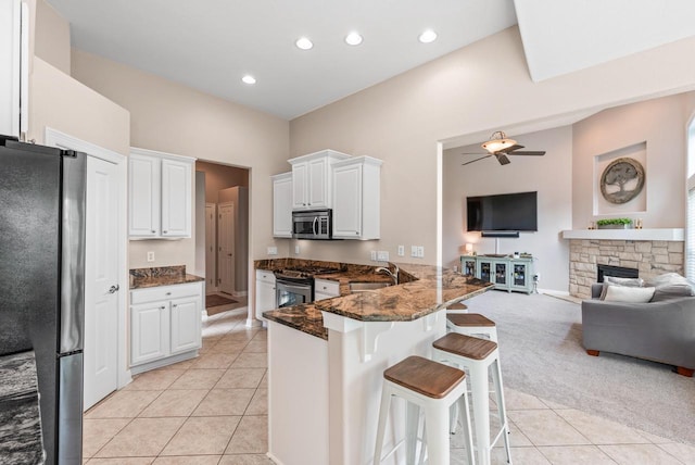 kitchen with a breakfast bar, dark stone countertops, kitchen peninsula, stainless steel appliances, and white cabinets