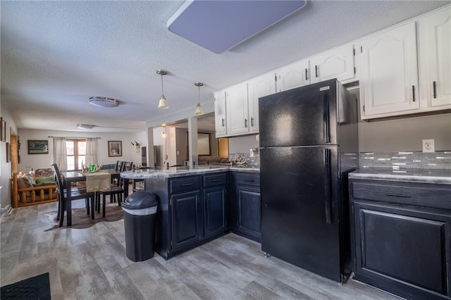 kitchen with light hardwood / wood-style flooring, white cabinetry, hanging light fixtures, black fridge, and kitchen peninsula