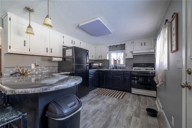 kitchen featuring white gas stove, black fridge, hanging light fixtures, kitchen peninsula, and white cabinets