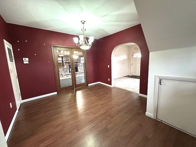 unfurnished dining area with french doors, dark hardwood / wood-style floors, a textured ceiling, and a notable chandelier