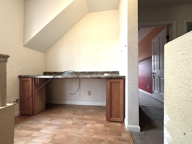 interior space with lofted ceiling, built in desk, and light hardwood / wood-style flooring