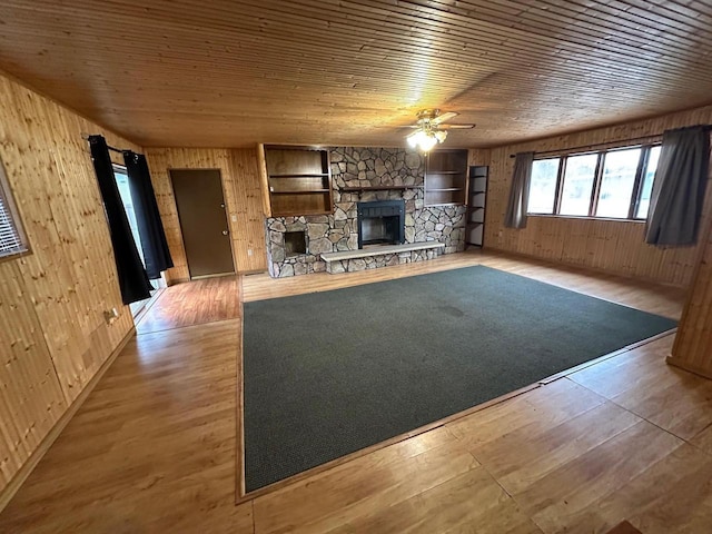 unfurnished living room featuring wood ceiling, ceiling fan, wooden walls, a fireplace, and light hardwood / wood-style floors