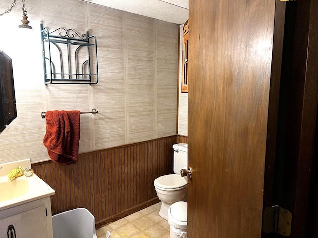 bathroom with vanity, wood walls, and toilet