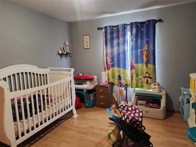 bedroom with light hardwood / wood-style flooring and a crib