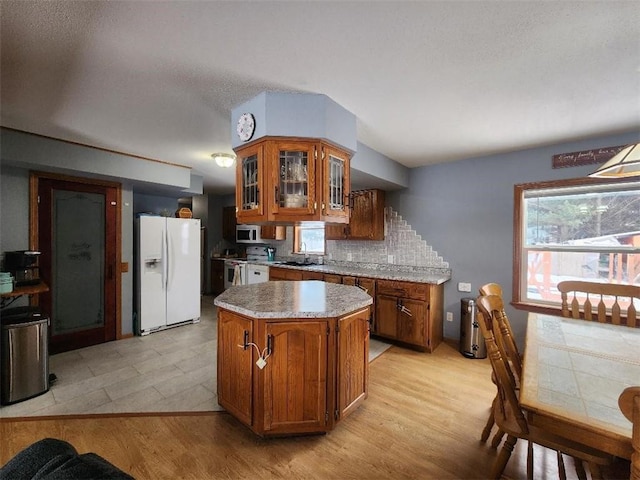 kitchen with decorative backsplash, white refrigerator with ice dispenser, a center island, light wood-type flooring, and electric stove