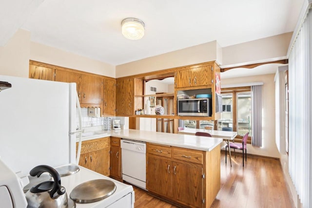 kitchen with white appliances, light hardwood / wood-style floors, kitchen peninsula, and decorative backsplash