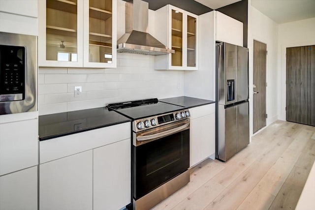 kitchen with white cabinetry, backsplash, light hardwood / wood-style floors, stainless steel appliances, and wall chimney exhaust hood