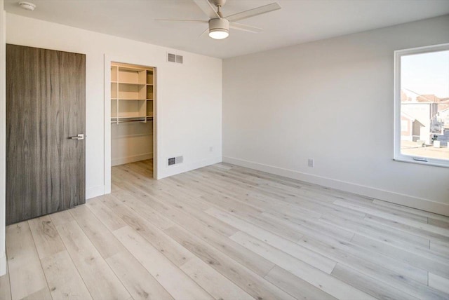 unfurnished bedroom with a walk in closet, light hardwood / wood-style floors, a closet, and ceiling fan