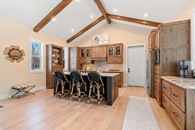 kitchen featuring a large island with sink, a kitchen breakfast bar, stainless steel appliances, light stone countertops, and decorative backsplash