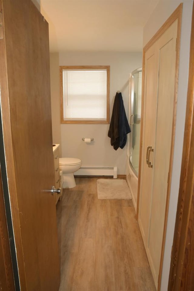 full bathroom with toilet, wood-type flooring, shower / bath combination with glass door, a baseboard radiator, and vanity