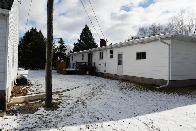 snow covered back of property with a wooden deck