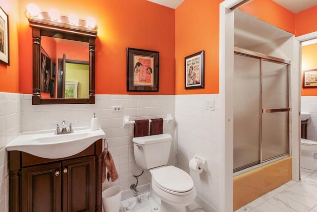 full bathroom with enclosed tub / shower combo, vanity, toilet, and tile walls