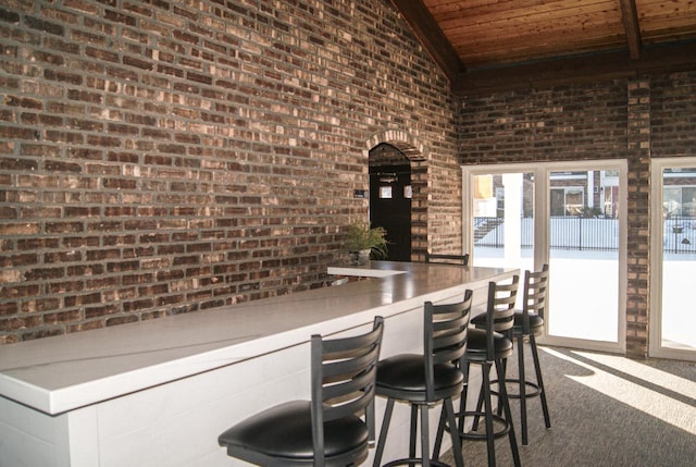 bar featuring lofted ceiling, wood ceiling, dark colored carpet, and brick wall