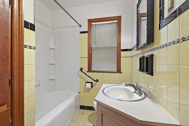 full bathroom with tile walls, vanity, toilet, tile patterned floors, and washtub / shower combination