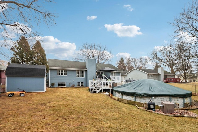 back of property featuring a swimming pool side deck, a shed, and a lawn