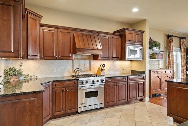 kitchen featuring appliances with stainless steel finishes, dark stone counters, decorative backsplash, light tile patterned floors, and custom range hood