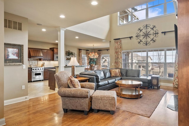 living room featuring decorative columns, a towering ceiling, an inviting chandelier, and light hardwood / wood-style floors