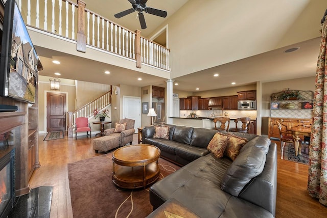 living room featuring hardwood / wood-style flooring, a towering ceiling, a premium fireplace, and ceiling fan