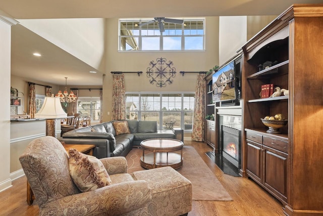 living room featuring a towering ceiling, ceiling fan with notable chandelier, and light hardwood / wood-style flooring