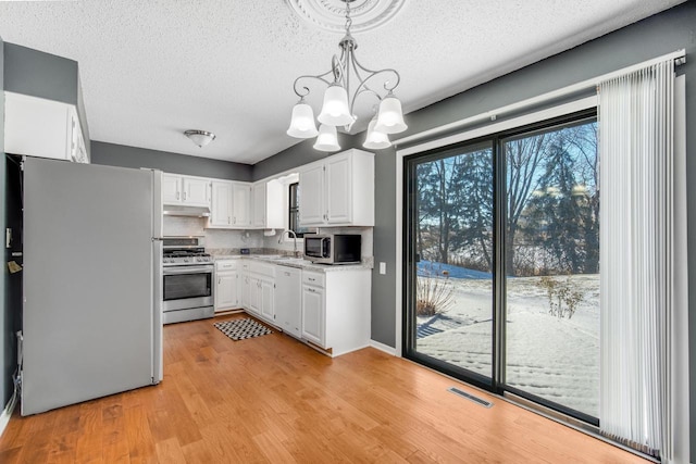 kitchen with decorative light fixtures, white cabinets, appliances with stainless steel finishes, a notable chandelier, and backsplash