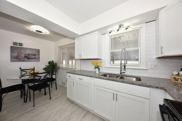 kitchen featuring stove, sink, dark stone countertops, and white cabinets